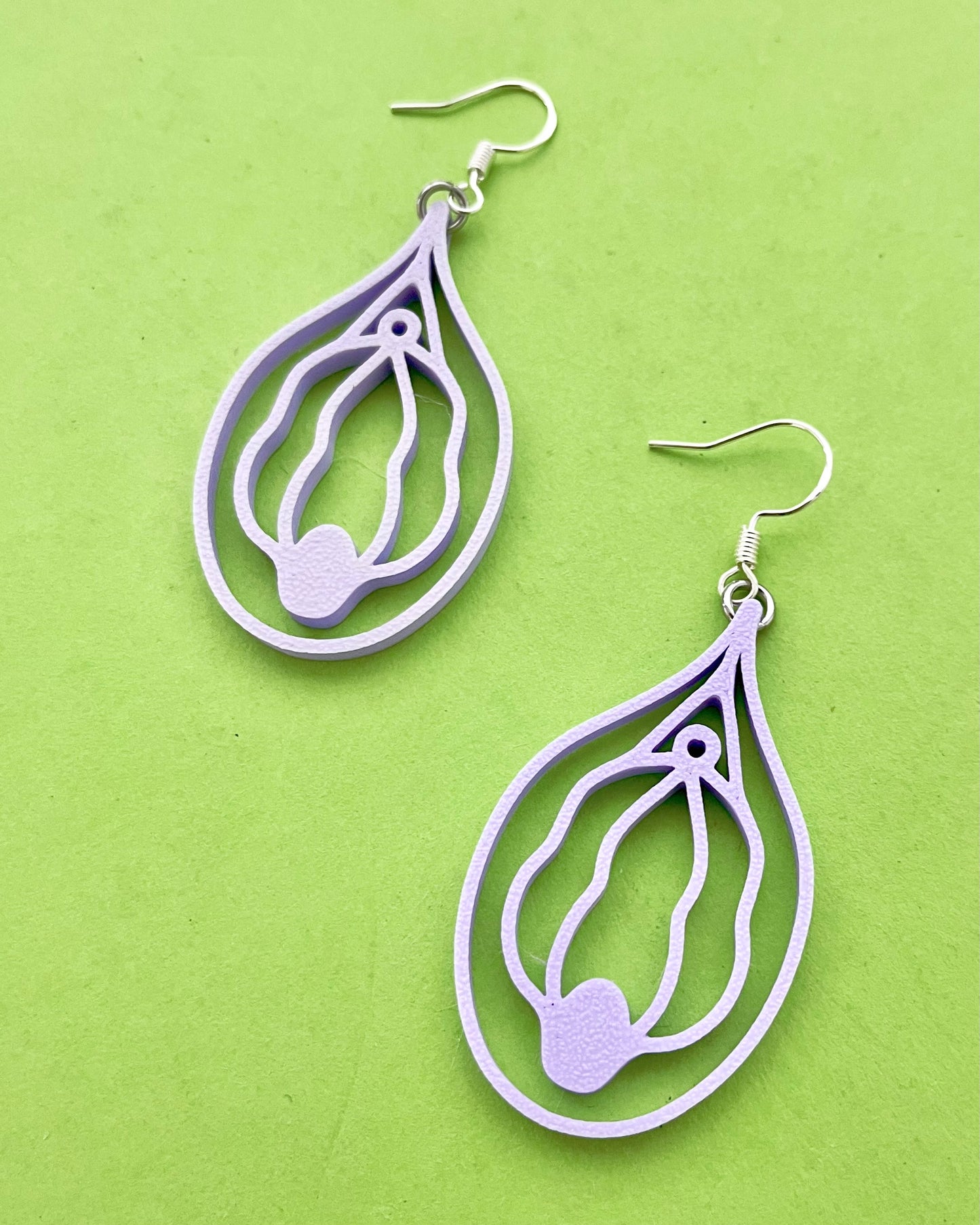 Pair of purple vulva shaped earrings on a green background