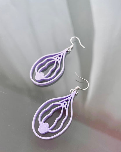 Pair of purple or lilac vulva shaped earrings on a reflective gray surface