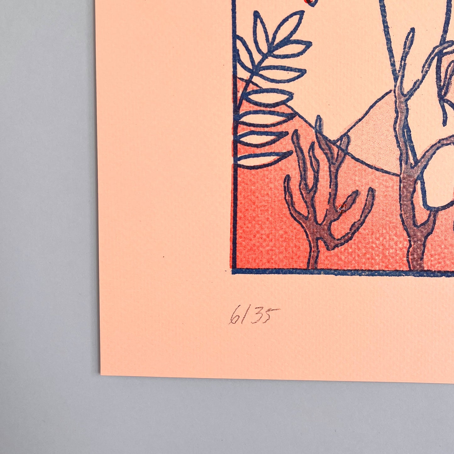 Art print with botanical design on a peach background, framed against a blue wall.