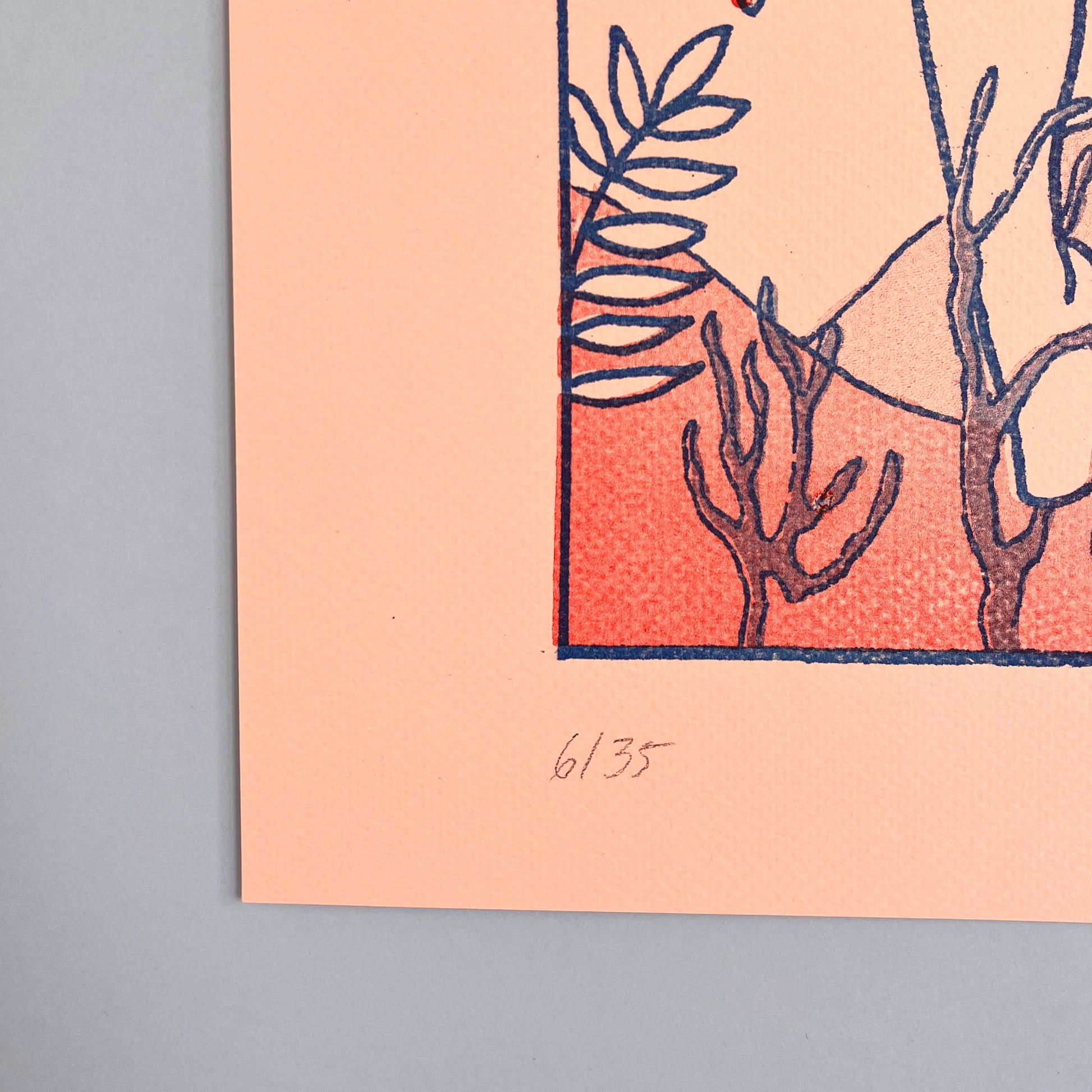 Art print with botanical design on a peach background, framed against a blue wall.